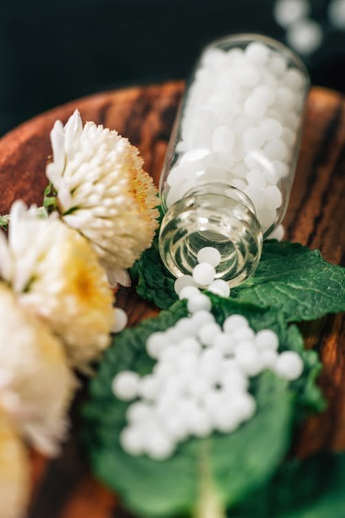 A close-up photo of a homeopath's hands holding a bottle of homeopathic remedies.